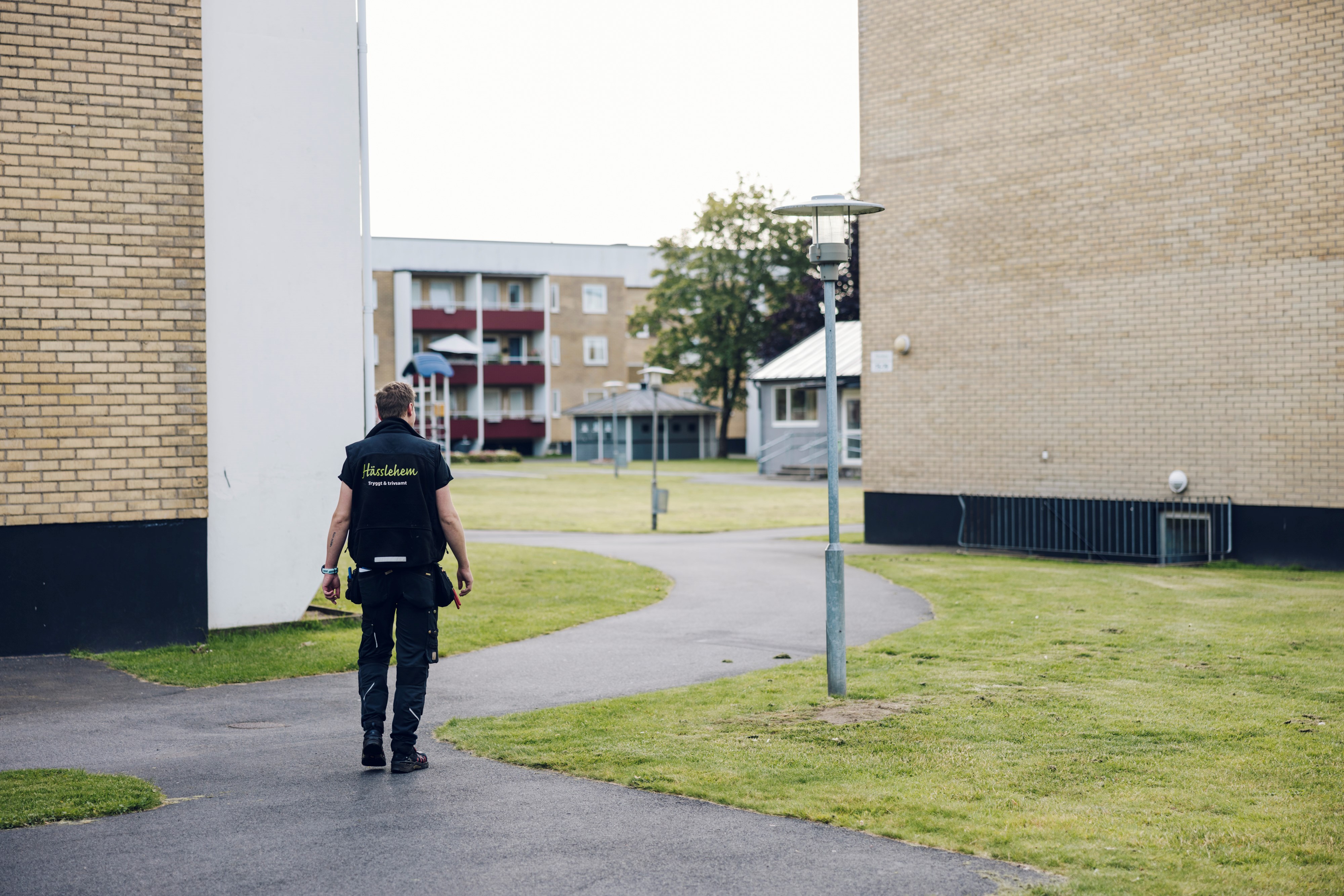 Man som går med ryggen mot kameran och mot innergård med höghus i gult tegel