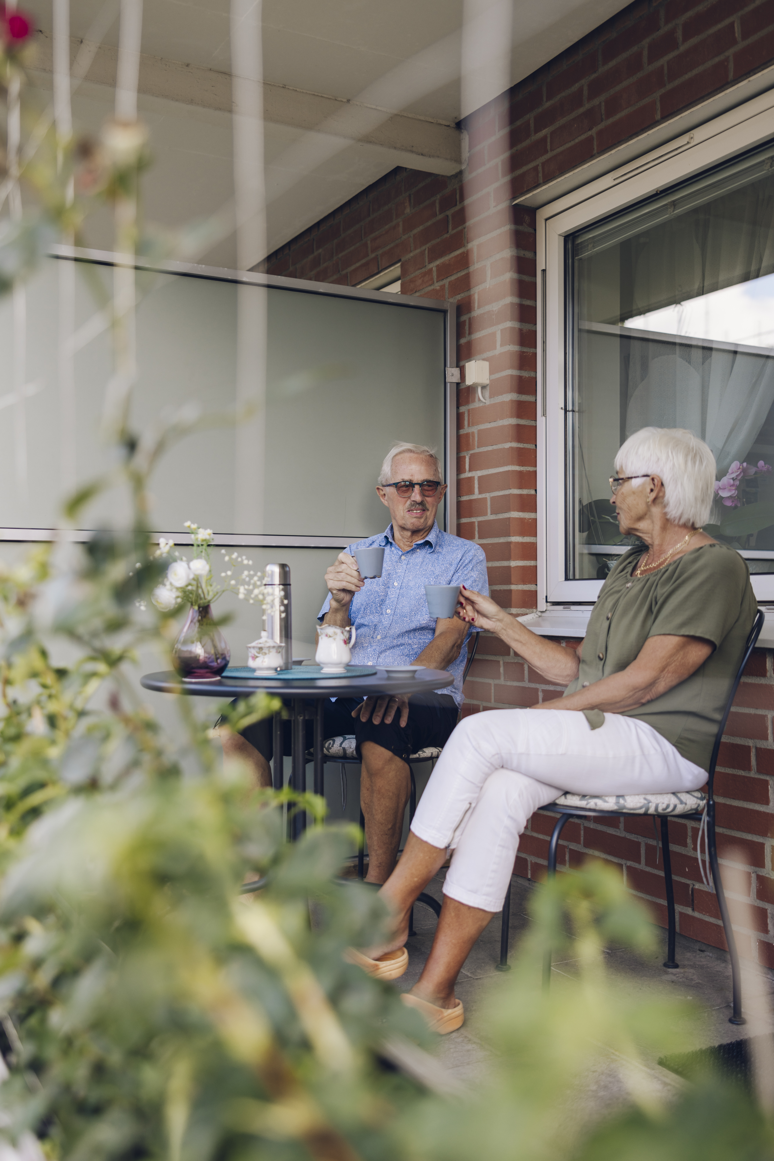 En kvinna och en man sitter på sin uteplats vid ett bord och dricker kaffe 