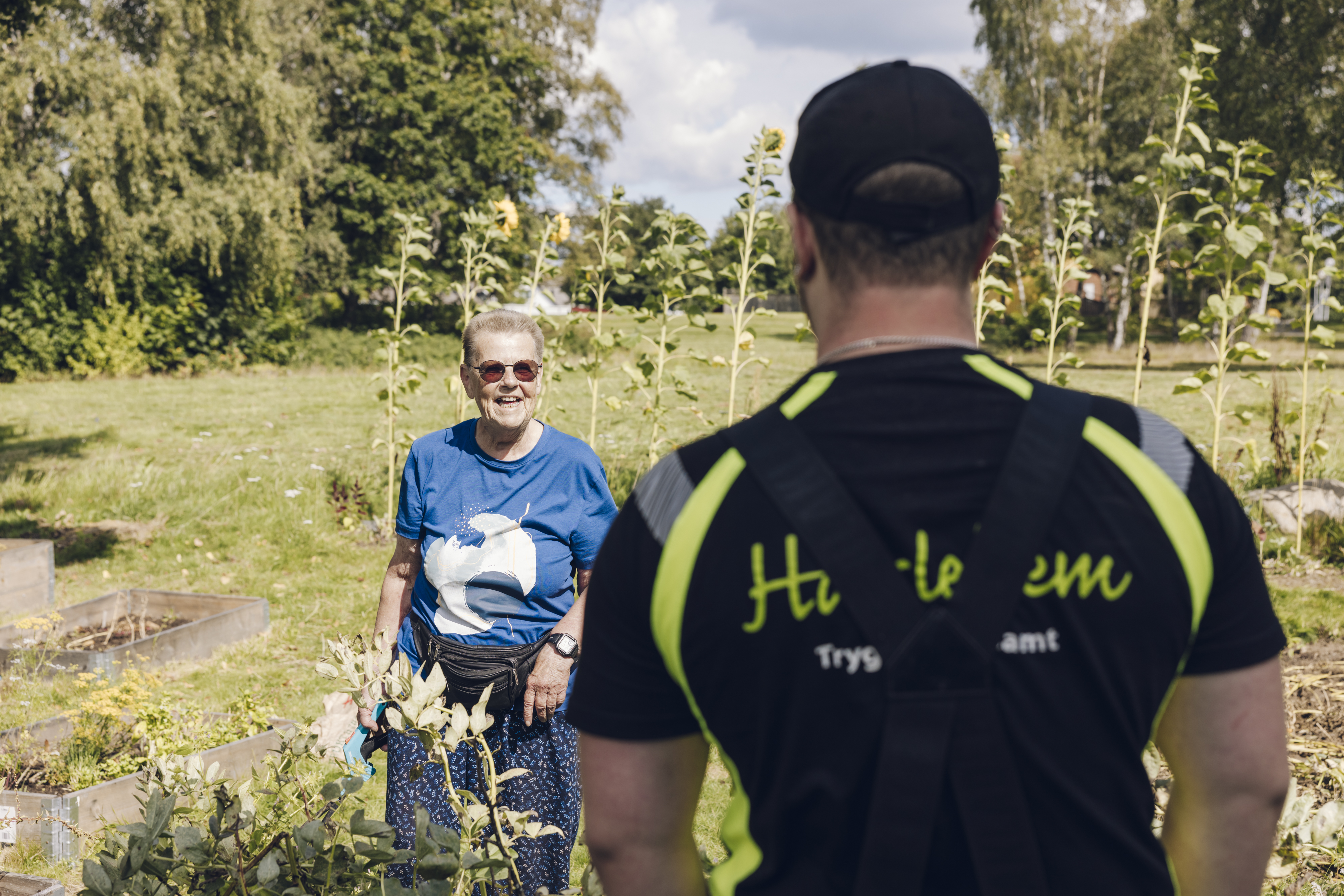 En kvinna står och pratar med en fastighetsskötare samtidigt som hon plockar blommor