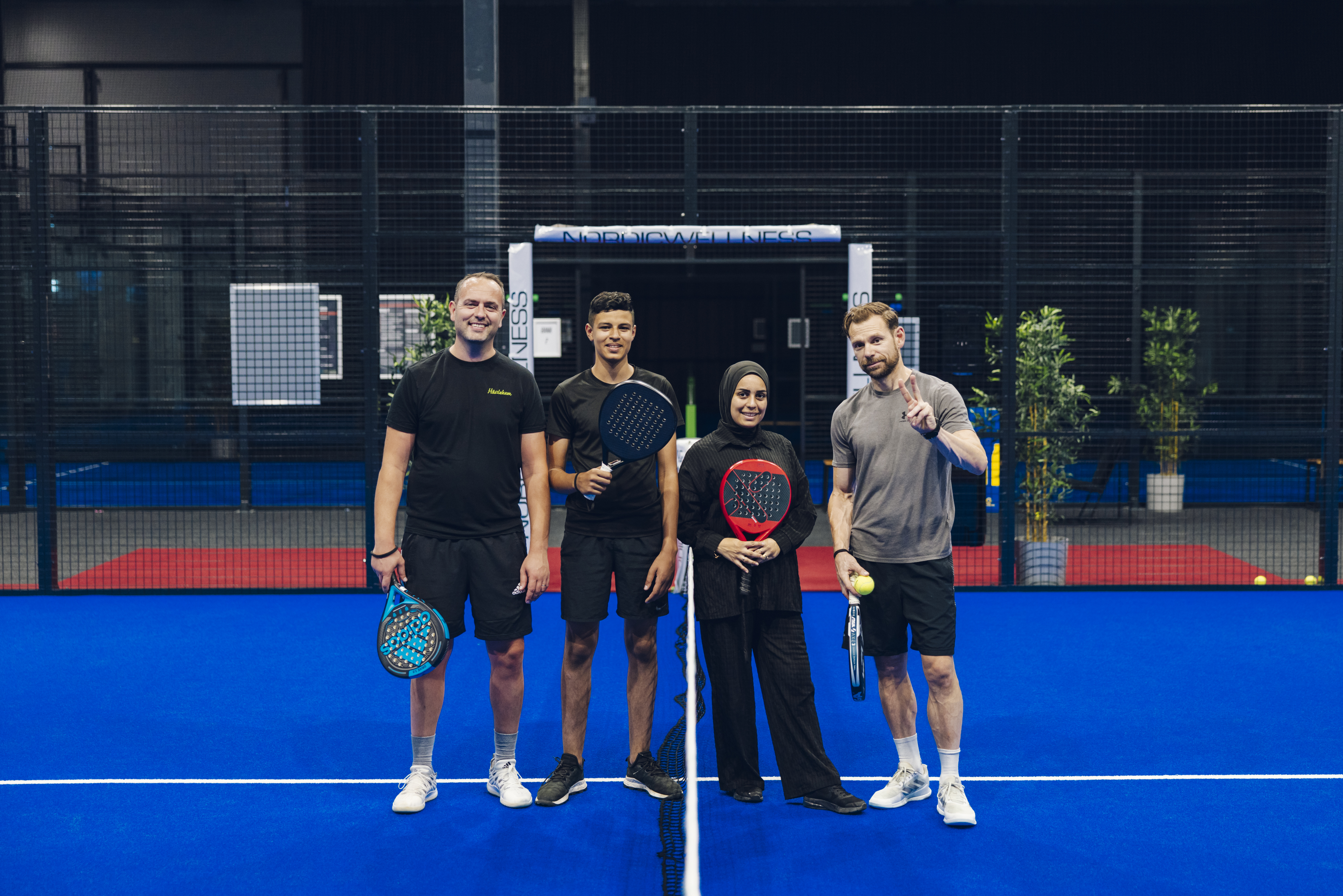 Tre killar och en tjej står uppradade på en padelbana med sin rack och ser glada ut