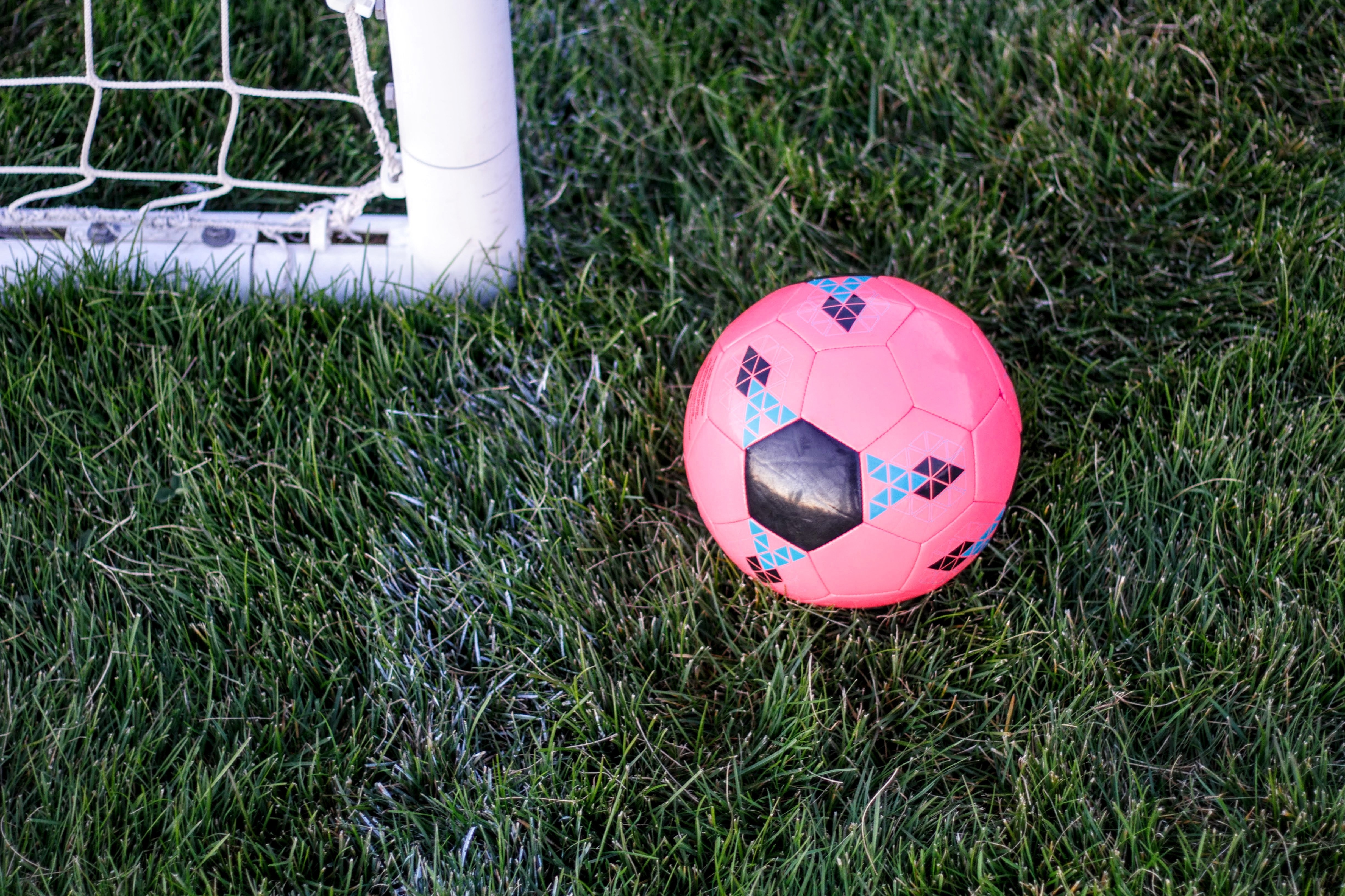 Rosa fotboll ligger på en gräsmatta bredvid ett vitt fotbollsmål