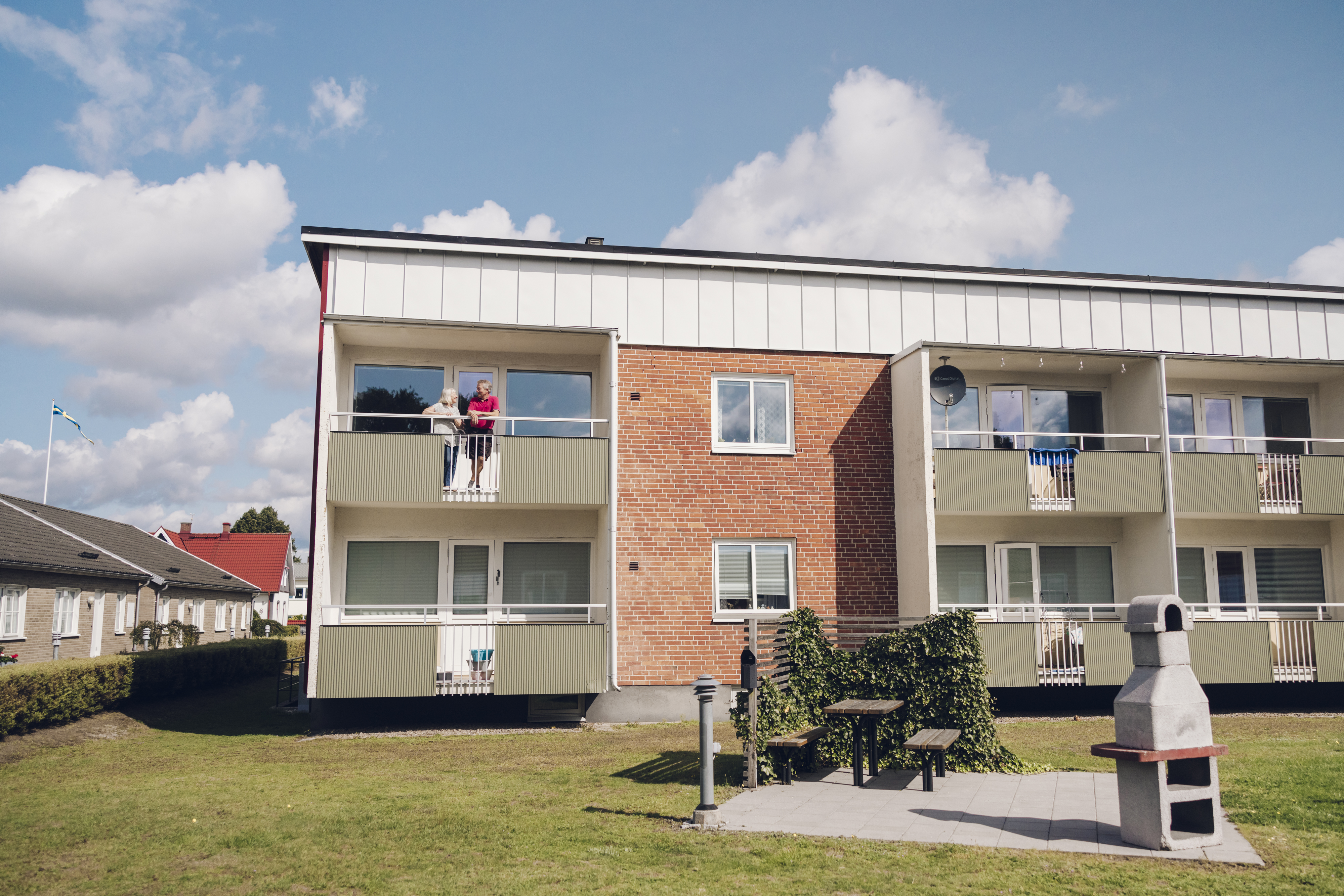 Par som står uppe på sin balkong på andra våningen i ett rött tegelhus