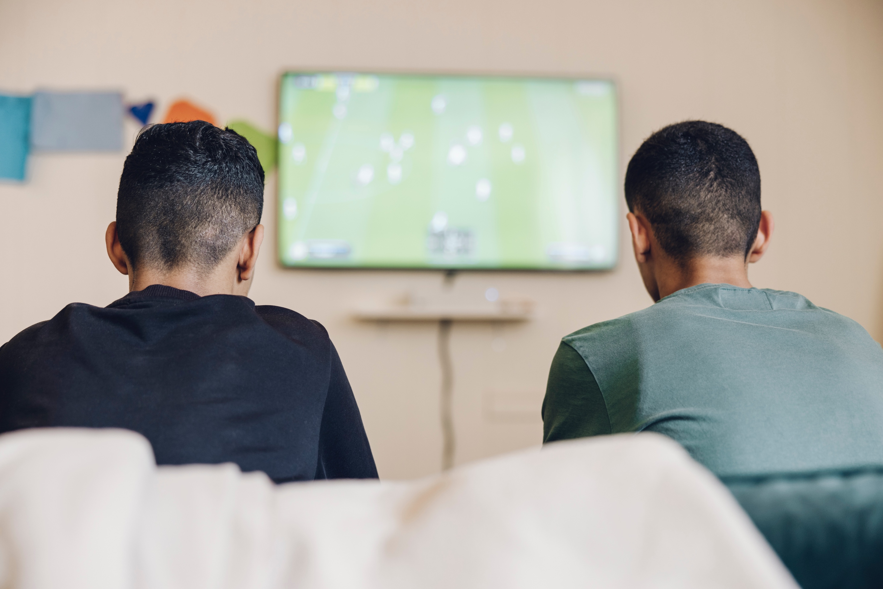 Två killar sitter med ryggen mot kameran och spelar TV-spel