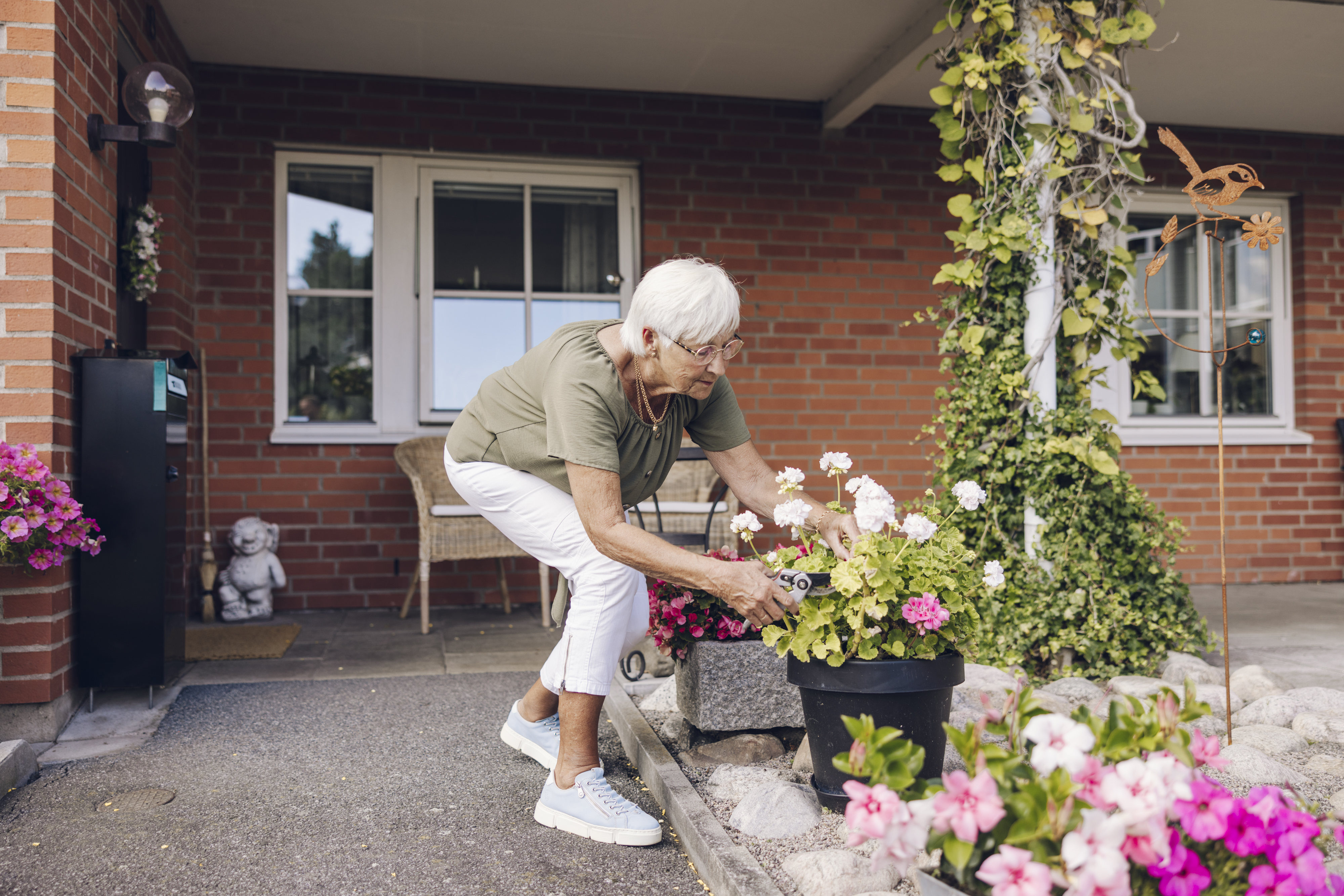 Kvinna i grön tröja och vita jeans står böjd över en blomma i klipper av grenar